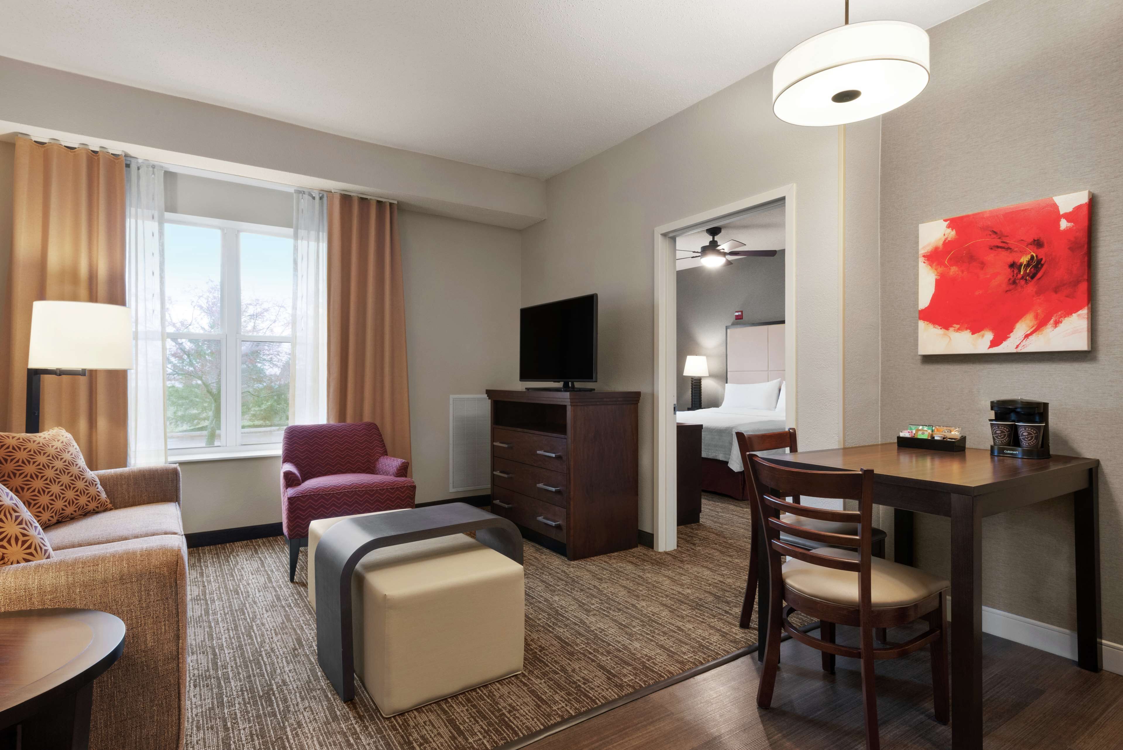 Habitación de hotel con sofá, una pequeña mesa, televisor, escritorio y sillas, y un cuadro en la pared.