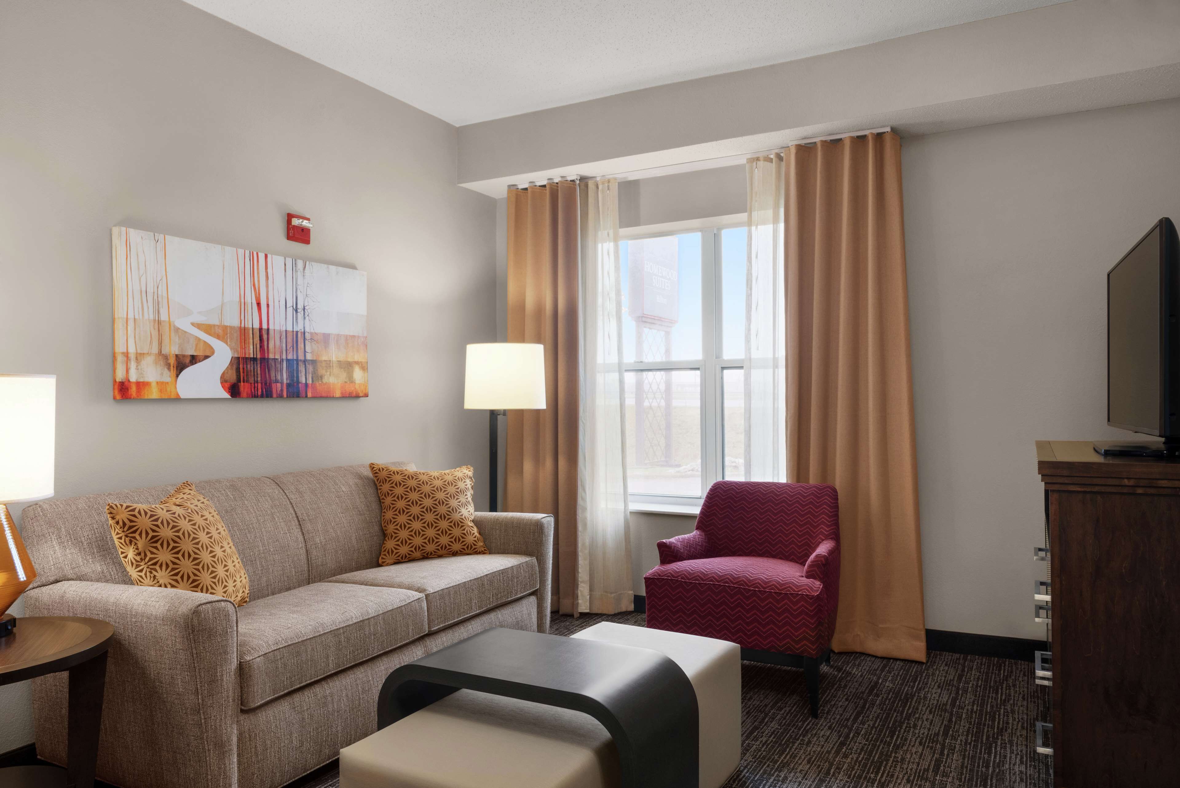 A hotel room with a sofa, armchair, TV, and artwork on the wall.