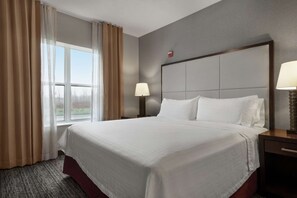 A hotel room with a large bed, a nightstand with a lamp, a window with curtains, and a view of the outdoors.