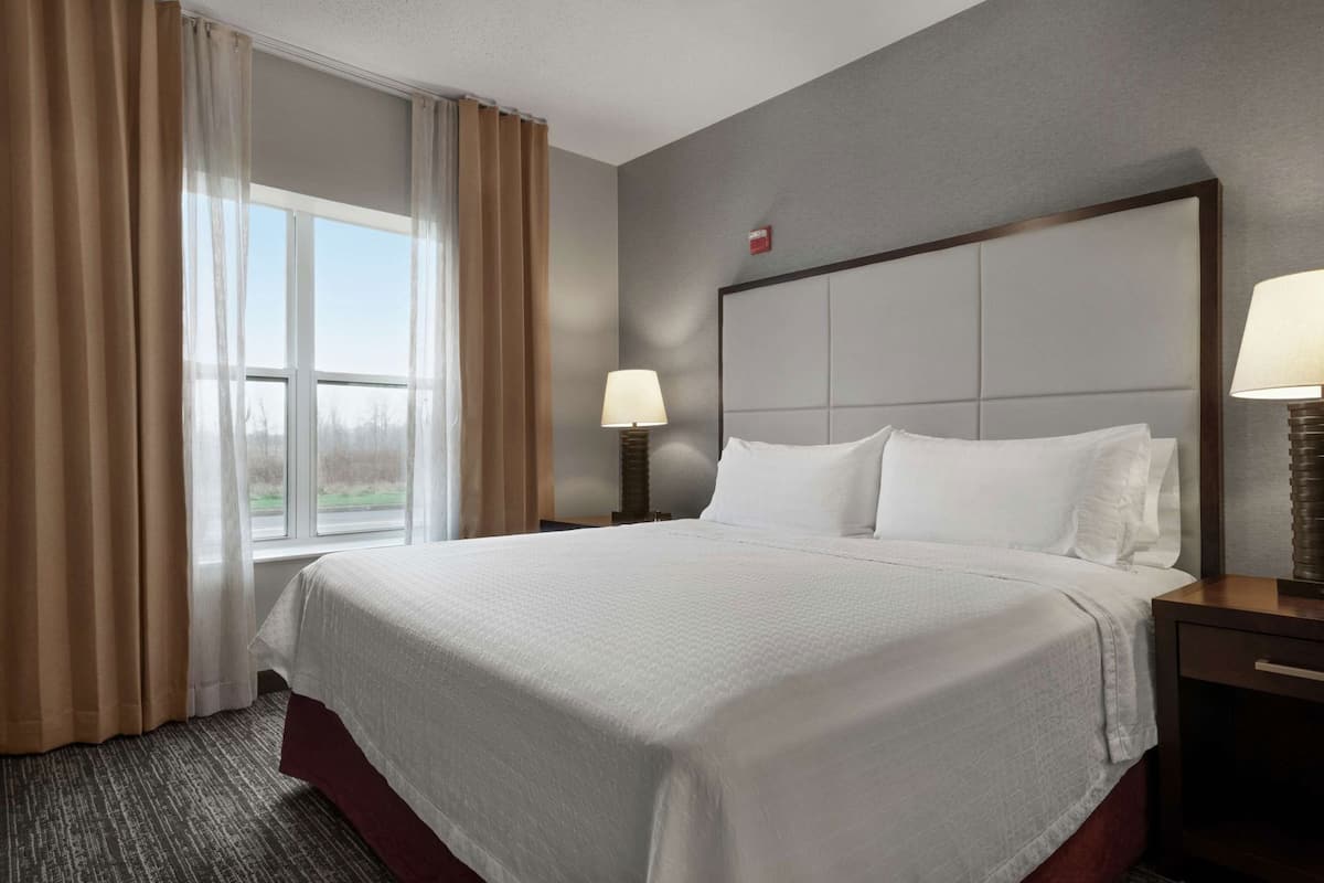 A hotel room with a large bed, two bedside lamps, a window with curtains, and a headboard.