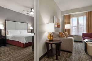 Quarto de hotel com uma cama, um sofá, uma mesinha e uma janela com cortinas.