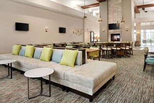 Um amplo hall de hotel com um sofá comprido, várias mesas e uma lareira.