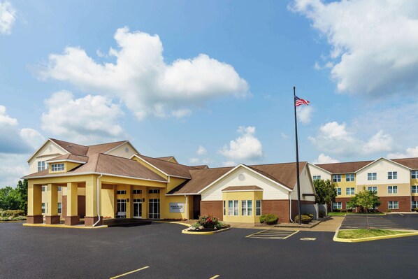 A hotel with a yellow facade, a parking lot, and an American flag.