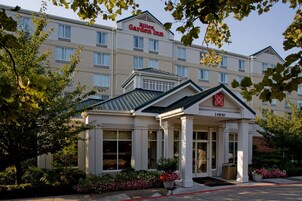 Un Hilton Garden Inn de estilo arquitectónico clásico, con una entrada destacada, un porche cubierto y un amplio parterre de flores.