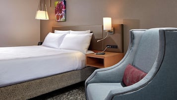A hotel room with a large bed, a nightstand, a lamp, and a chair.