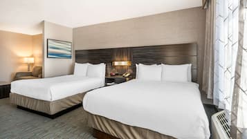 A hotel room with two beds, a nightstand with a lamp, a painting on the wall, and a window with curtains.