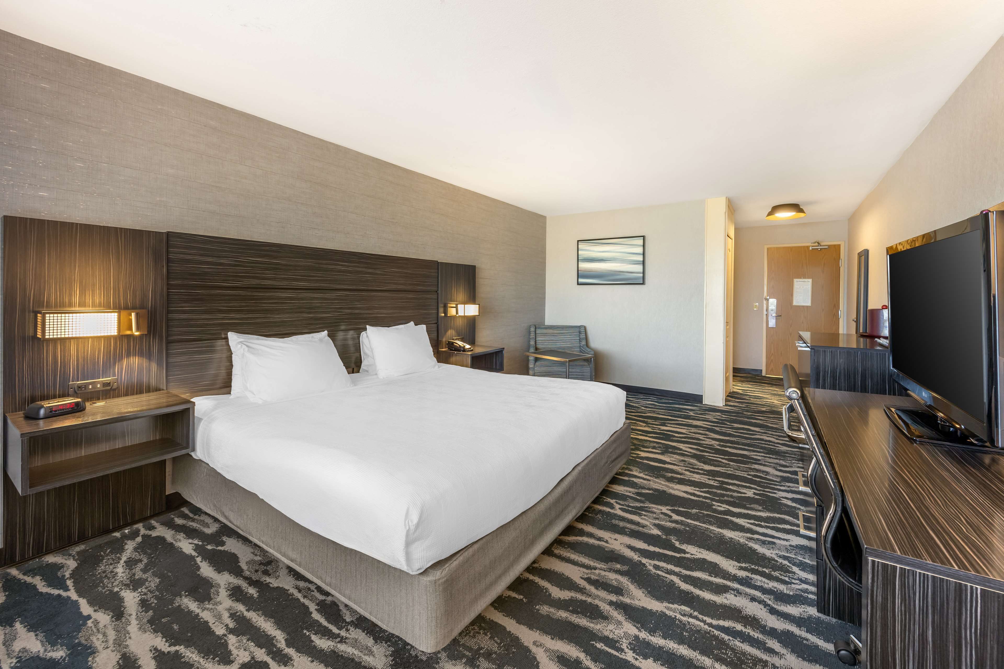 Habitación de hotel con una cama grande, un televisor de pantalla plana, un escritorio con una silla y una mesita de noche con lámpara.