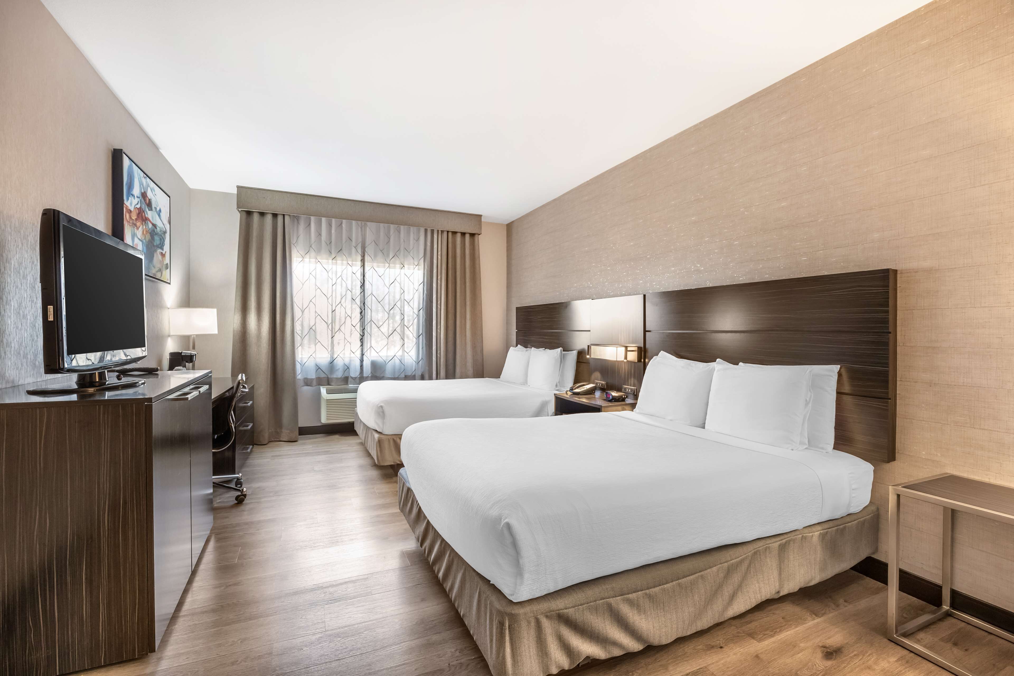 A hotel room with two beds, a desk with a TV, a lamp, and a window with curtains.
