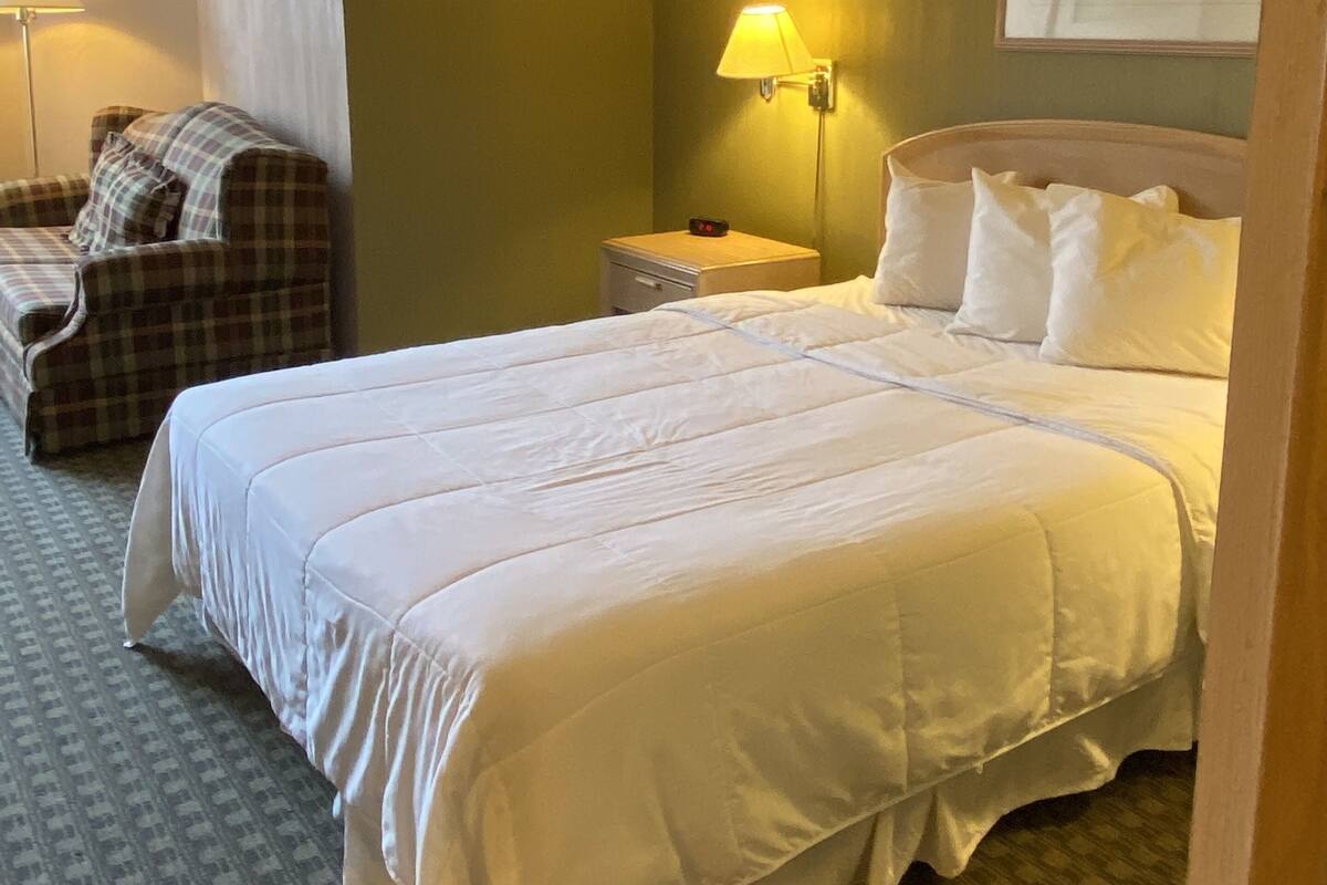 A hotel room with a large bed, a chair, a nightstand, and a lamp.