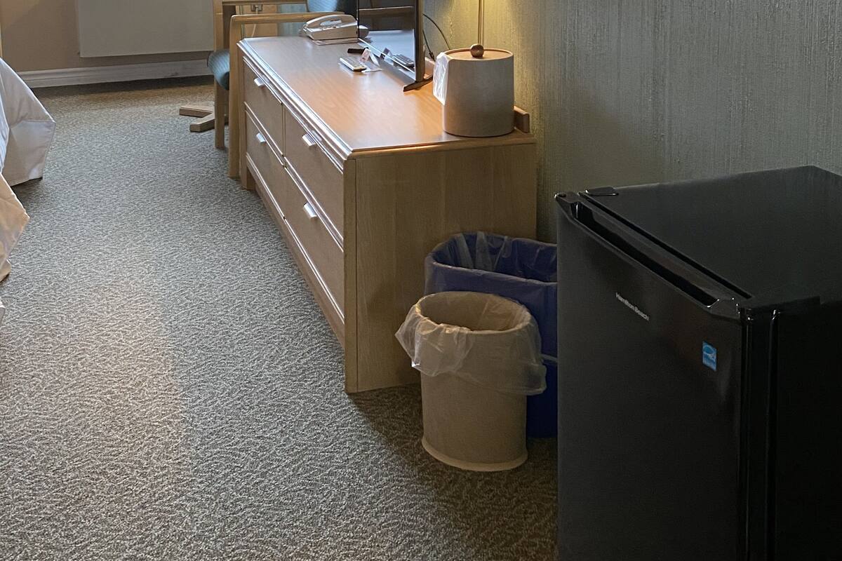 A hotel room with a desk, chair, lamp, and a black refrigerator.