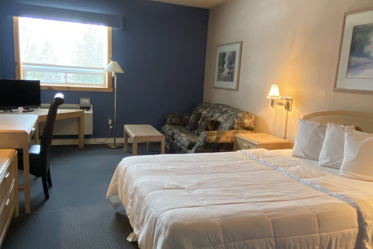A hotel room with a bed, desk, chair, and a window.