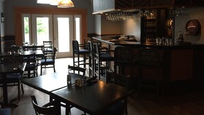 Un restaurant doté d’un bar, de tables et de chaises en bois, et d’une grande fenêtre laissant entrer la lumière naturelle.
