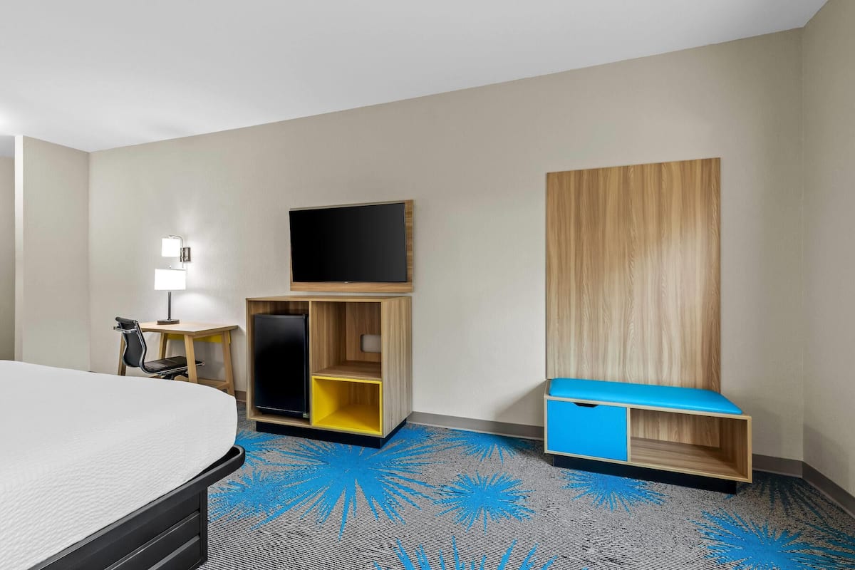 A hotel room with a bed, a TV, a desk, and a storage unit.