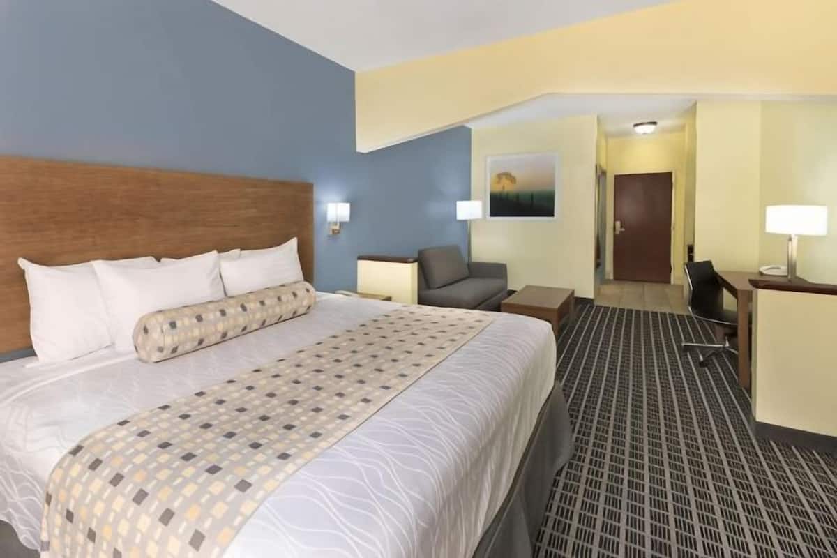 A hotel room with a large bed, a desk, a chair, and a door leading to a hallway.