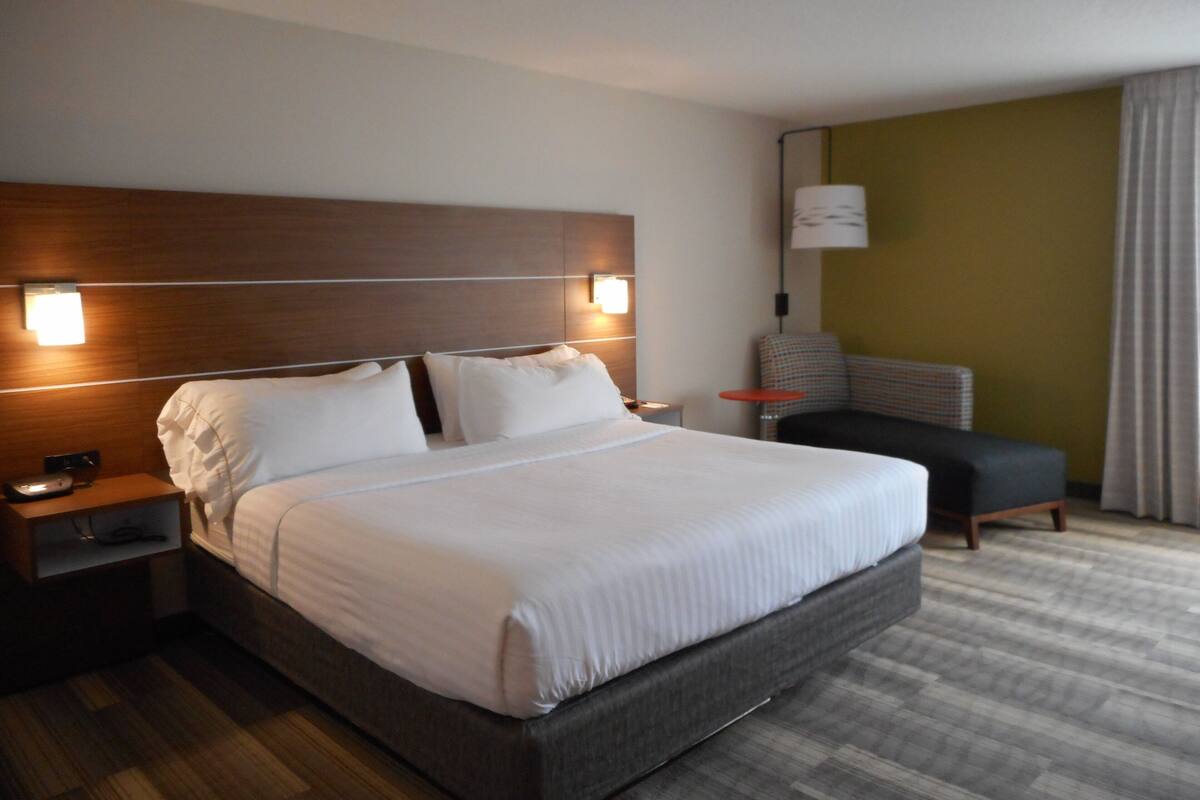 A hotel room with a large bed, a nightstand, a chair, and a lamp.