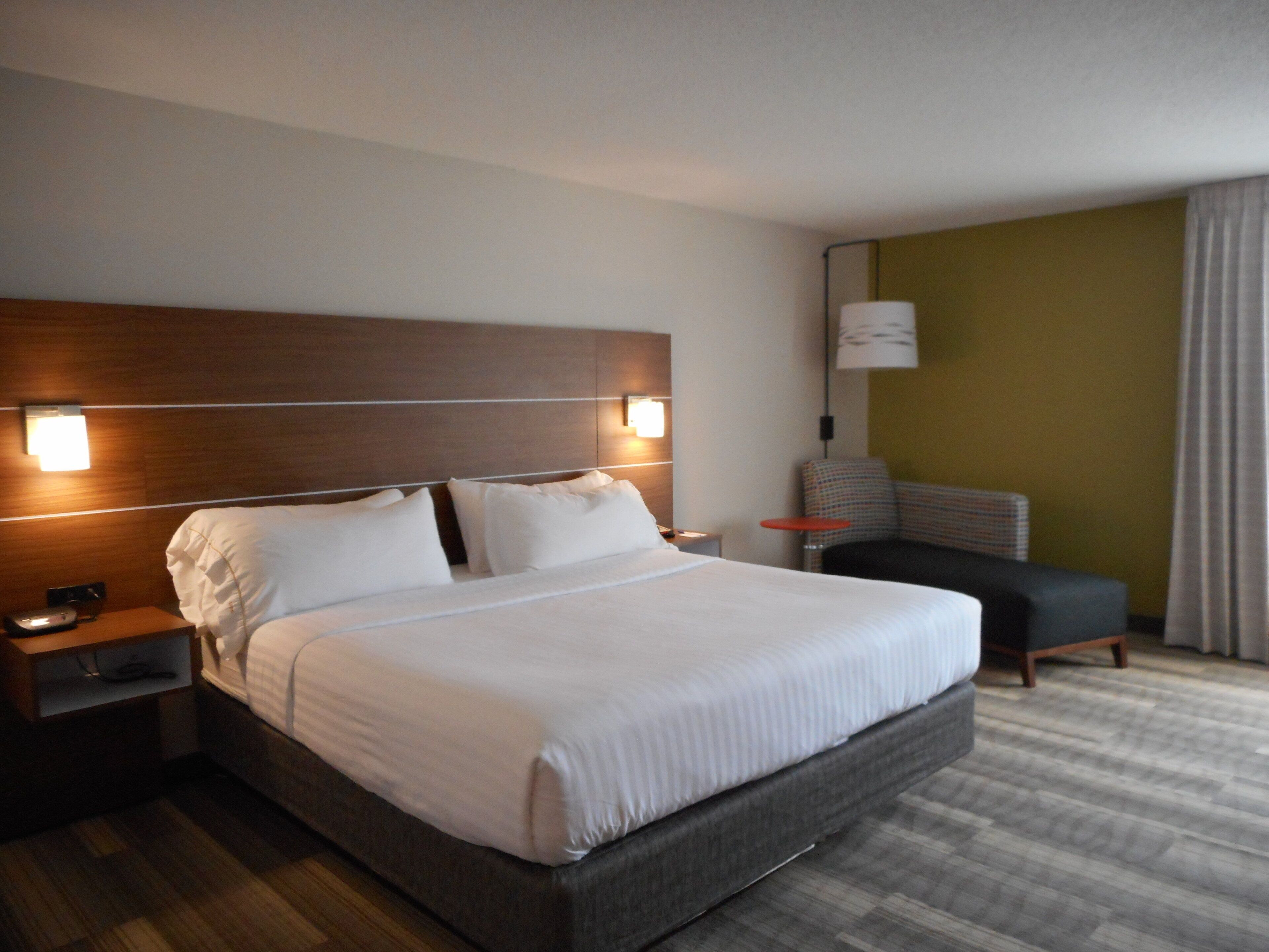 A hotel room with a large bed, a nightstand, a chair, and a lamp.