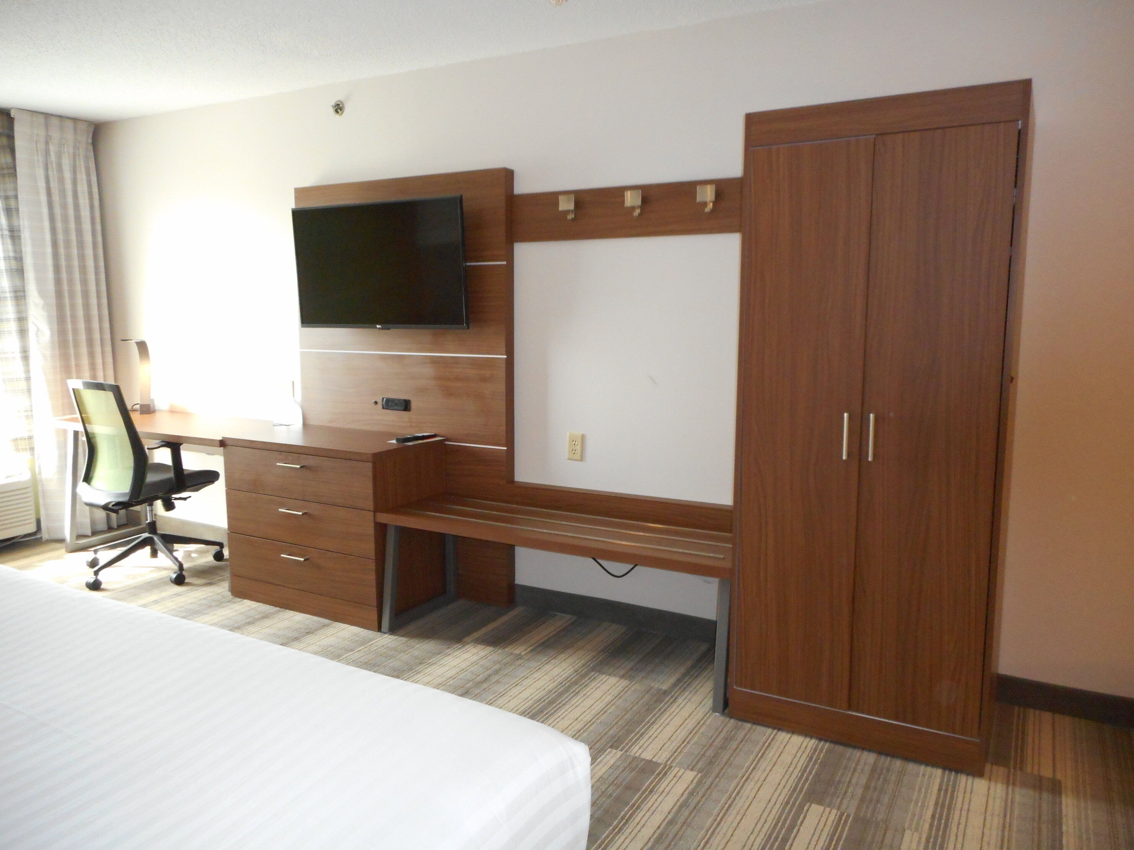 A hotel room with a bed, a desk with a chair, a TV, and a wardrobe.
