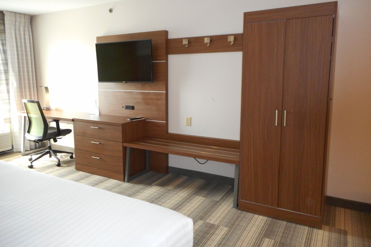 A hotel room with a bed, a desk with a chair, a TV, and a wardrobe.