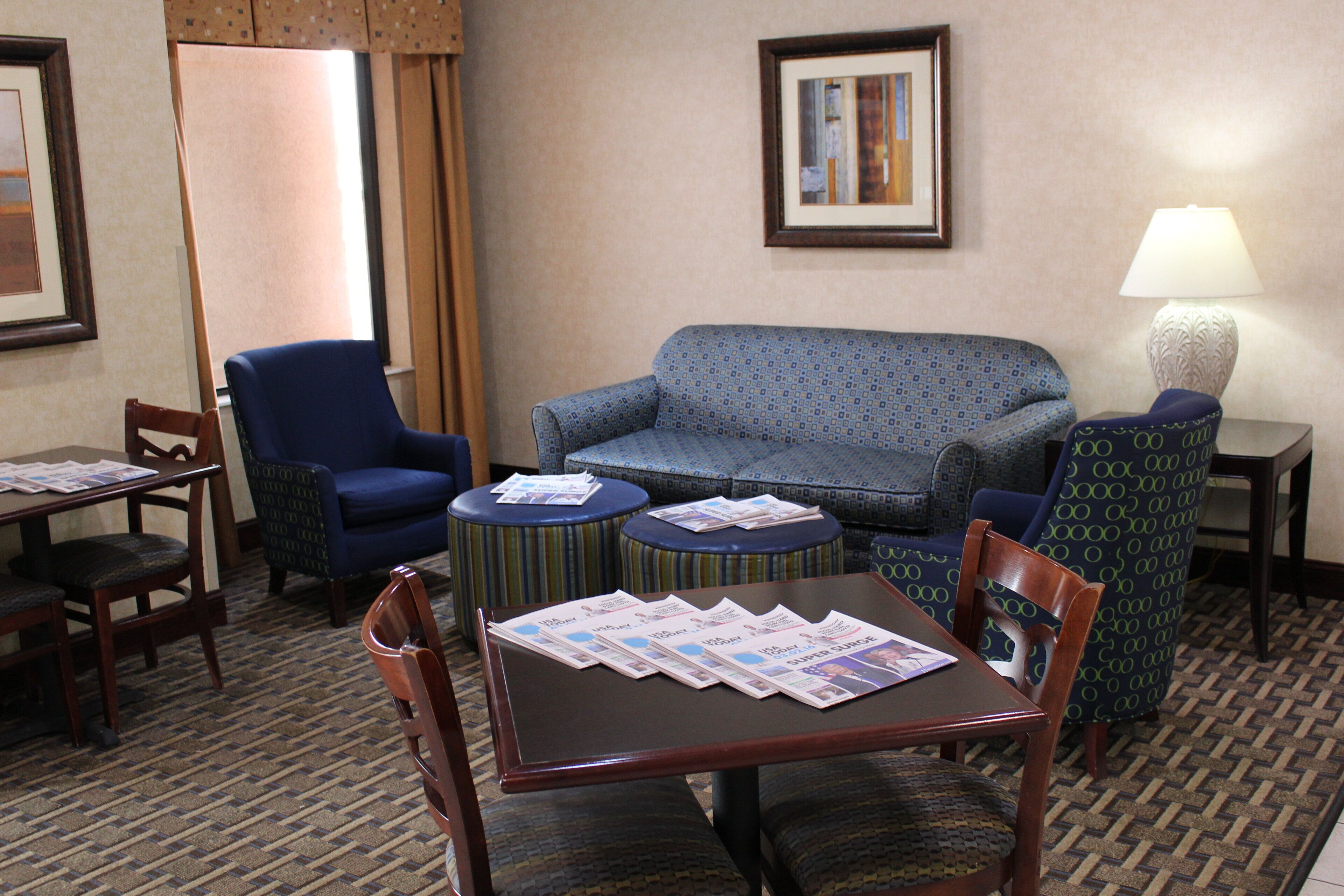Habitación de hotel con sofá, sillones, una mesa de comedor con sillas y una lámpara.