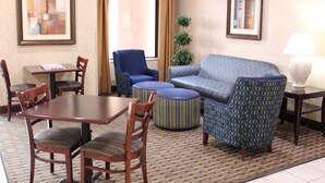A hotel room with a dining table, chairs, a sofa, ottomans, a lamp, and framed pictures on the walls. - Holiday Inn Express Kansas City-Liberty by IHG (Kansas City)