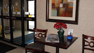 Un vestíbulo de hotel con mostrador de recepción, sillas, una obra de arte enmarcada en la pared y una puerta con señales de precaución.