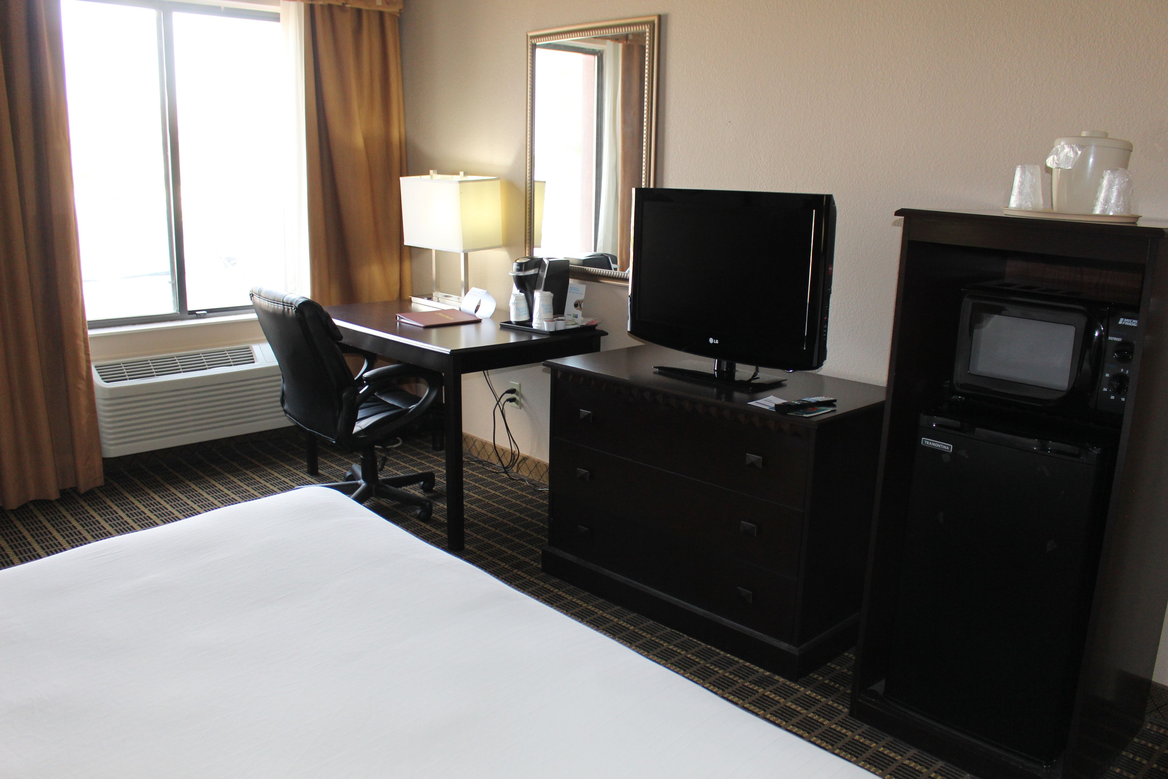 A hotel room with a bed, a desk with a computer, a television, a microwave, and a coffee maker.