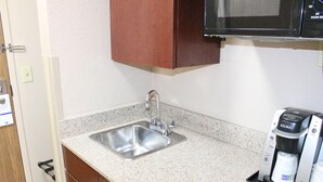 A kitchen with a stainless steel sink, a Keurig coffee maker, and wooden cabinets. - Holiday Inn Express Kansas City-Liberty by IHG (Kansas City)