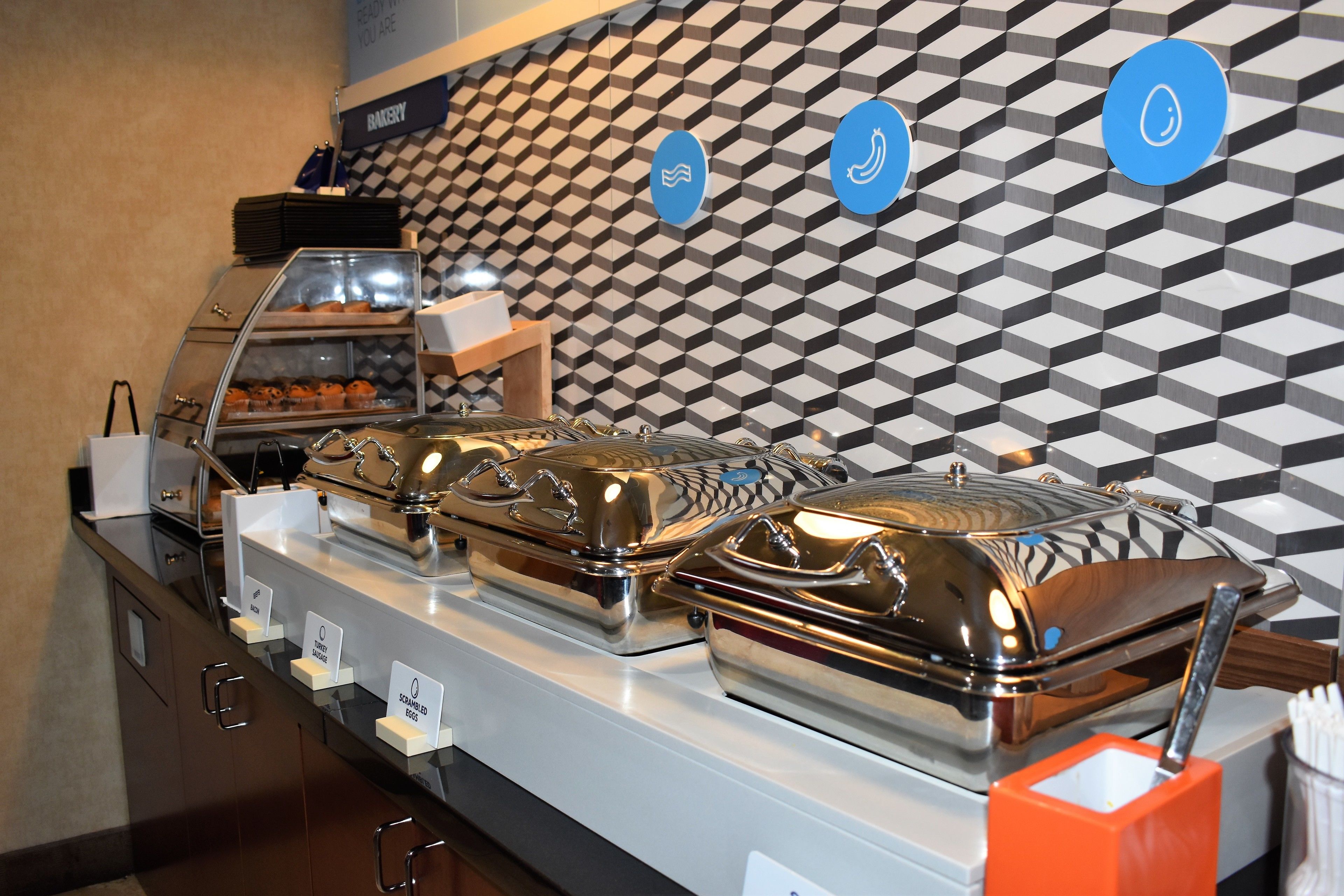 Montaje de bufé con varias estaciones de comida, un mostrador de recepción y una pared con patrón geométrico.