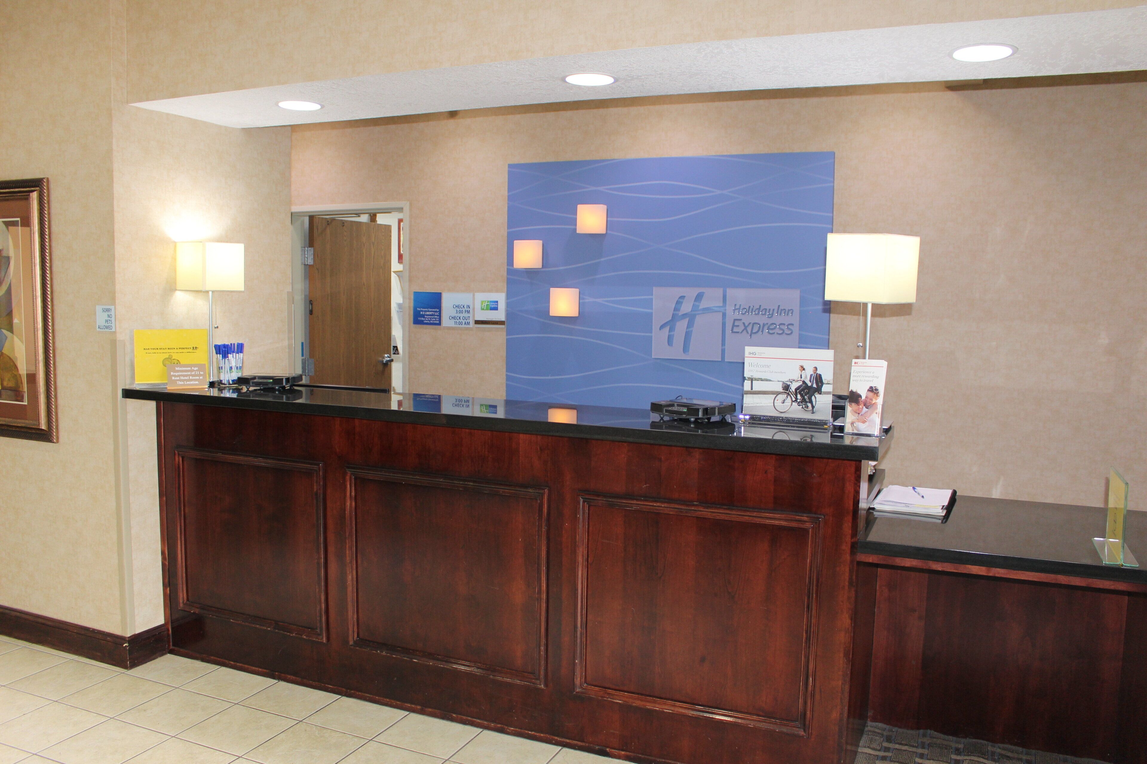 A hotel reception desk with a wooden finish, a check-in counter, and a blue wall with the hotel name.