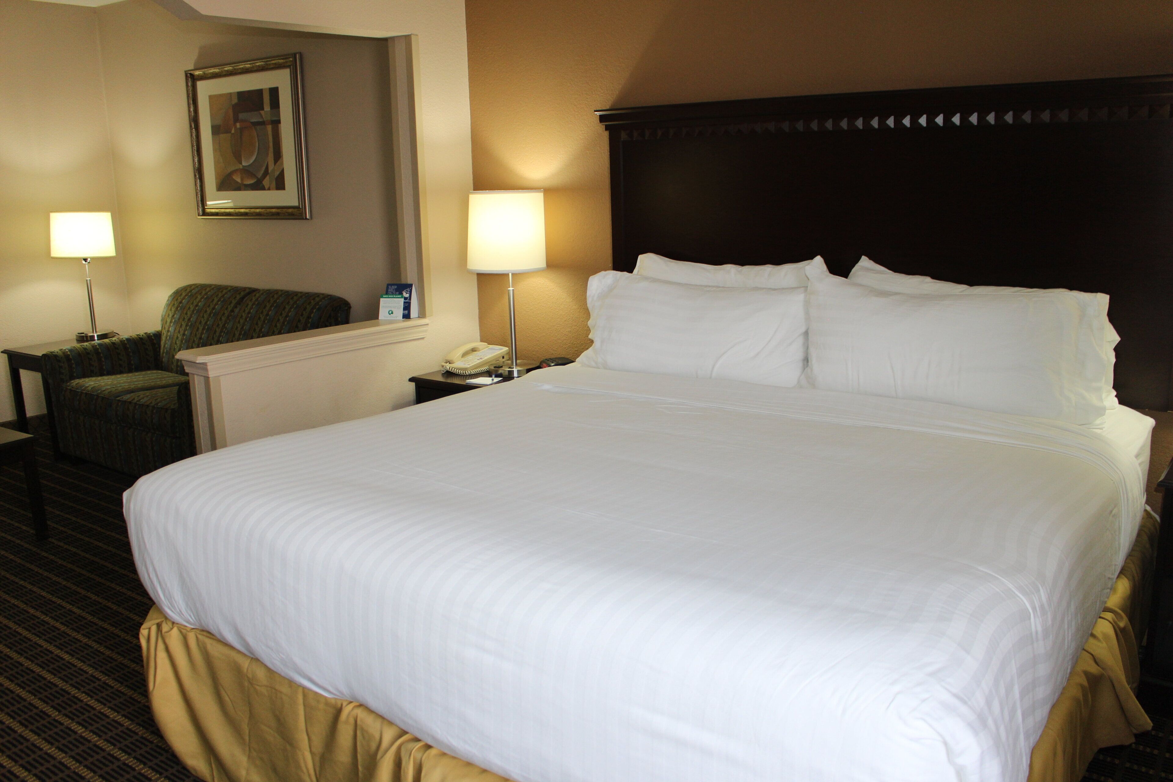 Habitación de hotel con una cama grande, dos lámparas de noche, un teléfono, una silla y un cuadro en la pared.