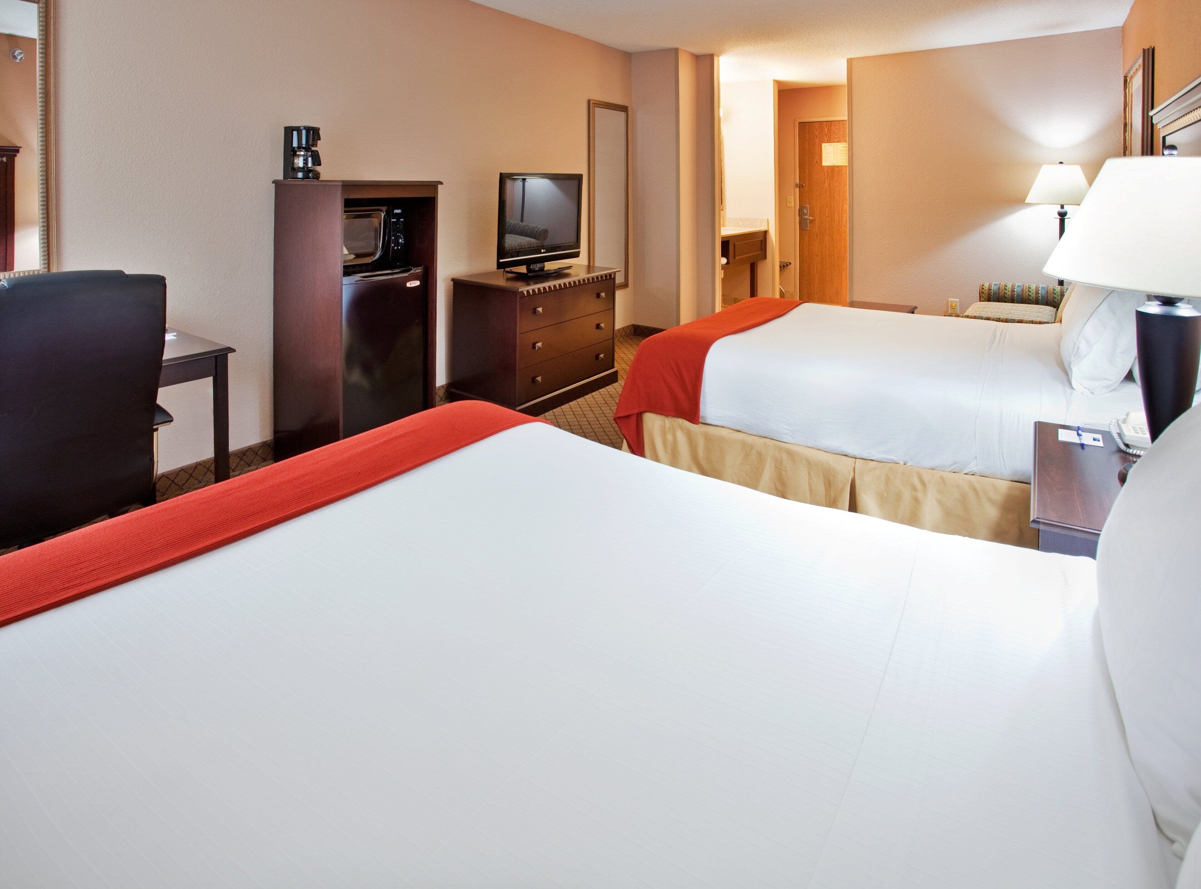 Una habitación de hotel con dos camas, un escritorio con computadora, televisor y cafetera.