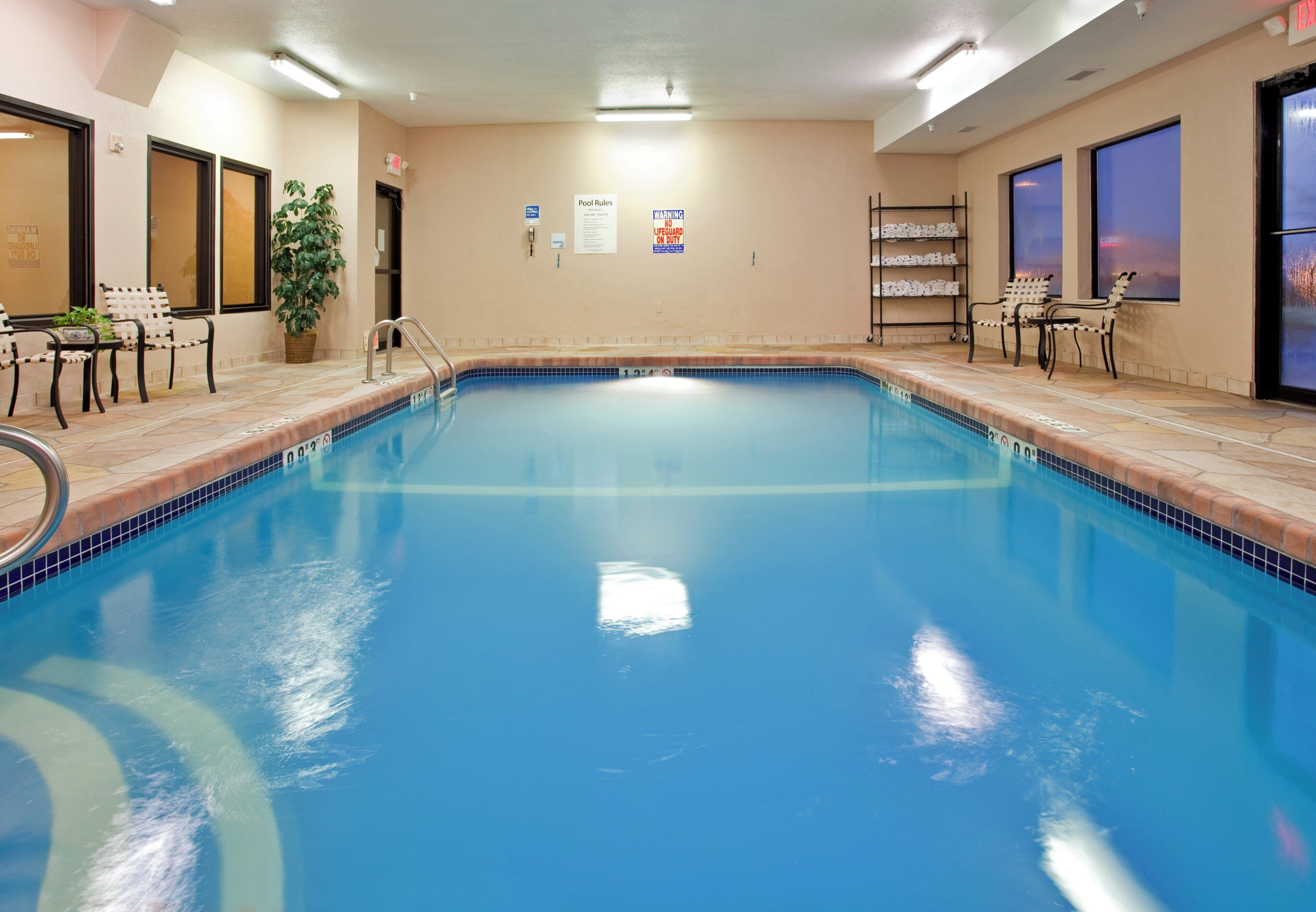 An indoor swimming pool with tiled edges, a lifeguard chair, and a sign indicating pool rules.