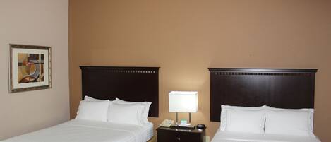 Habitación de hotel con dos camas, una mesita de noche con lámpara y un cuadro en la pared.