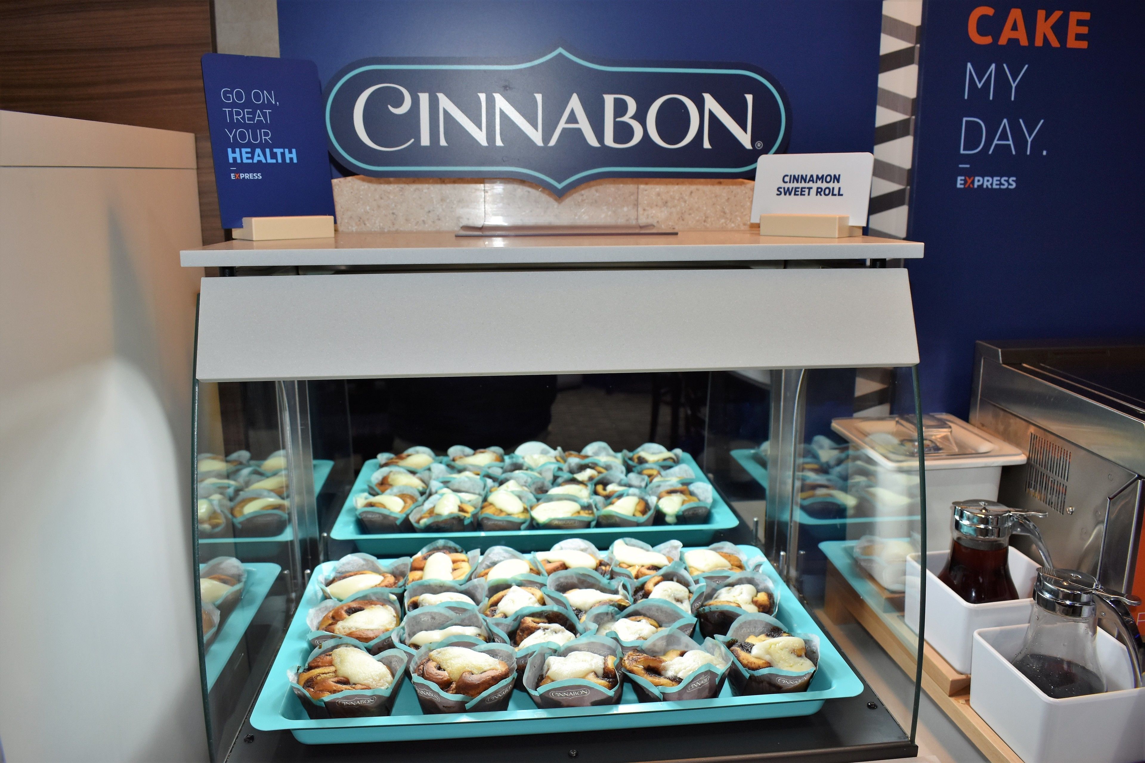 Una vitrina llena de varios pasteles y un letrero encima que dice "CINNABON".