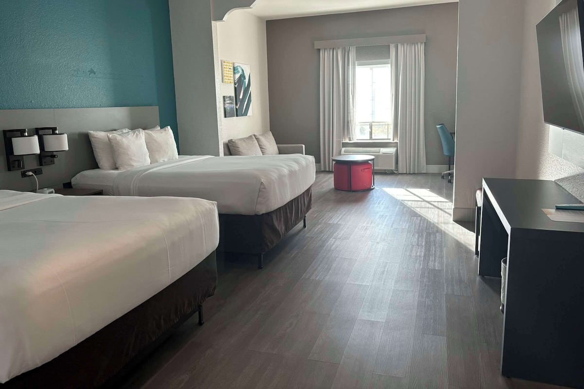 A hotel room with two beds, a desk, a chair, a small table, and a window with curtains.