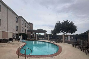 Una piscina con un pabellón cubierto, sillas de descanso y un área cercada.