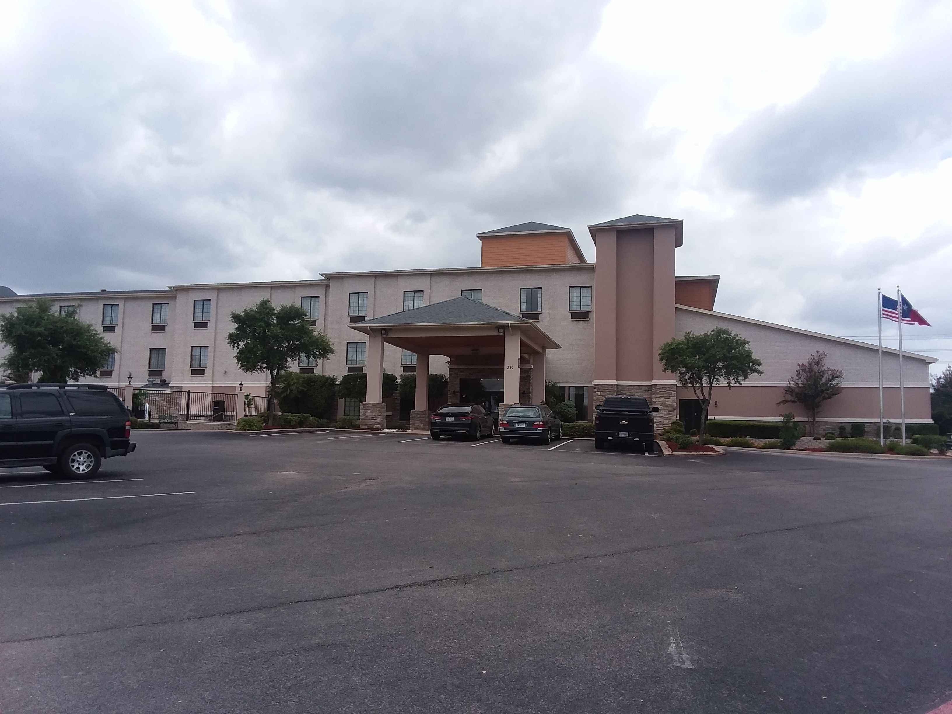 A multi-story hotel with a covered entrance, parking lot, and American flag.