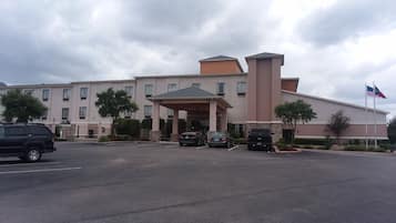 A multi-story hotel with a covered entrance, parking lot, and American flag.
