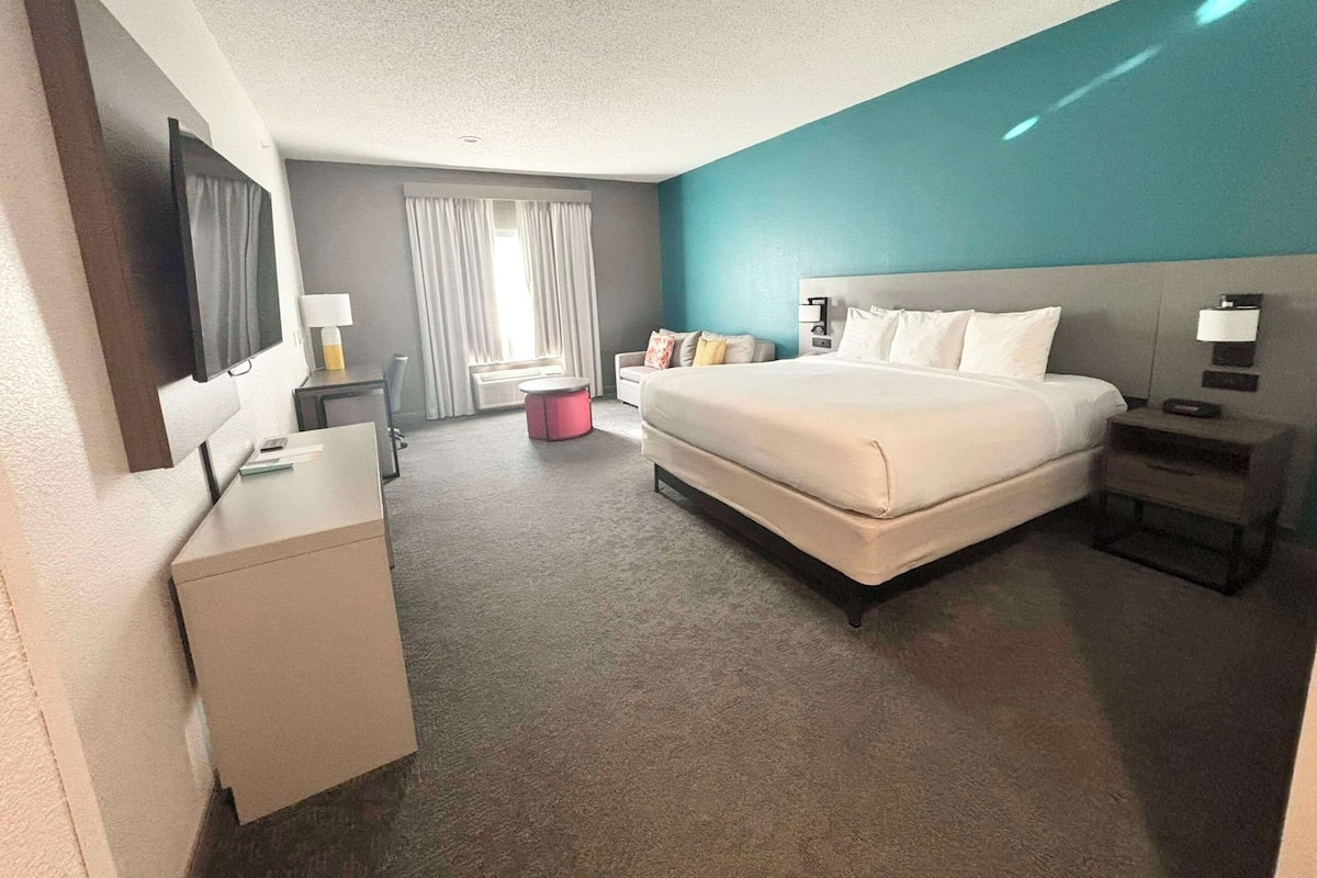 A hotel room with a large bed, a desk, a chair, a TV, and a window with curtains.