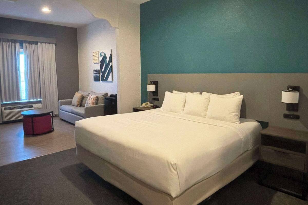 A hotel room with a large bed, a sofa, a small table, and a nightstand with a lamp.