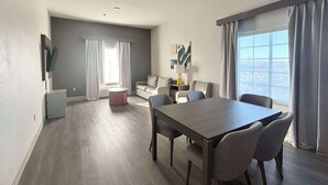 Un salon moderne avec un coin repas, des murs gris et une grande fenêtre avec des rideaux.