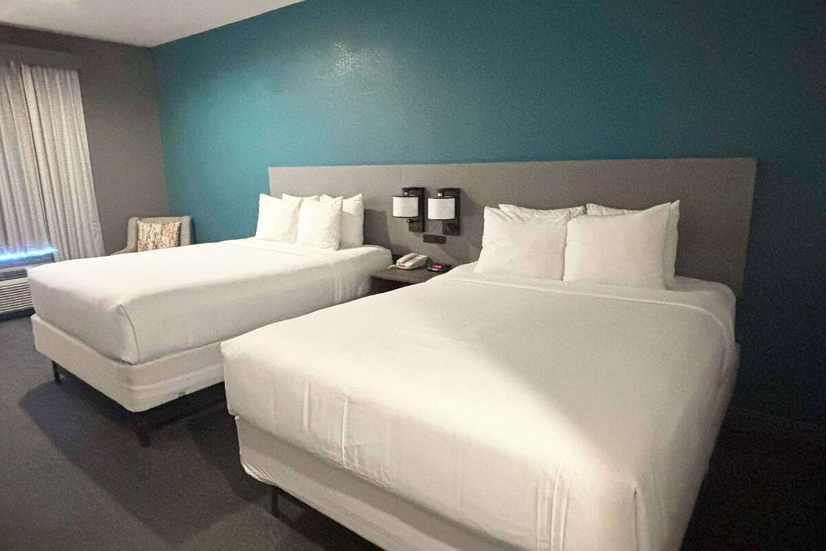 A hotel room with two beds, a nightstand with a phone, and a wall-mounted light fixture.