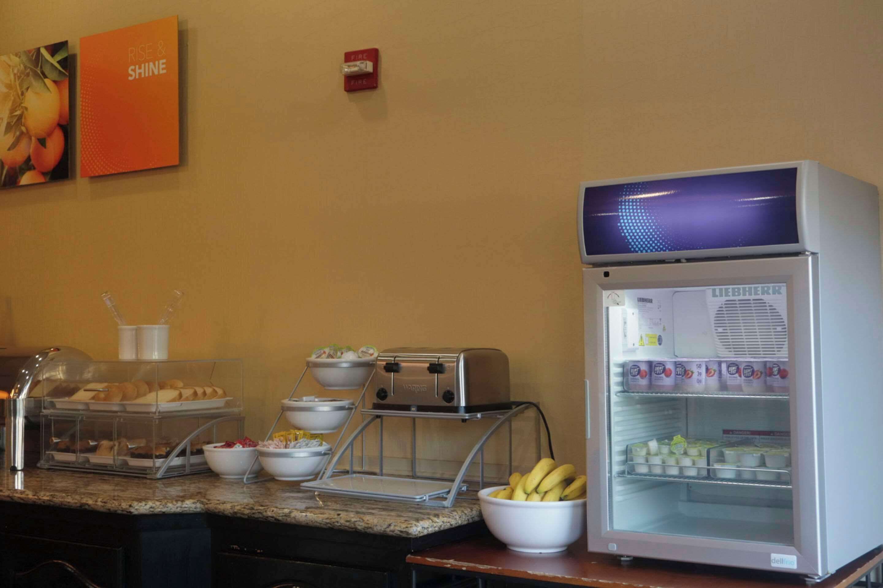 A breakfast buffet with a self-service station, a refrigerator with dairy products, and a fruit bowl.
