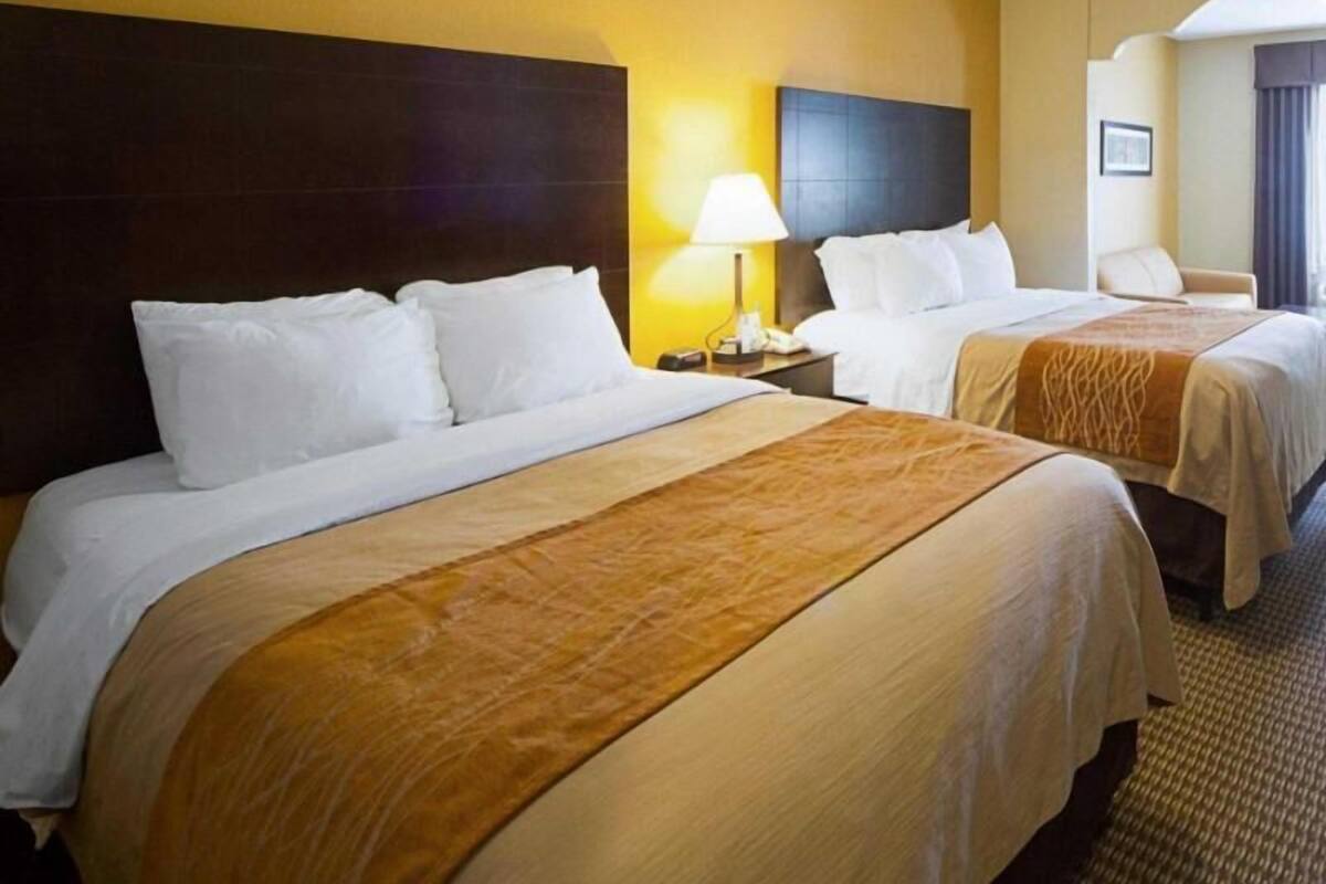 Ein Hotelzimmer mit zwei Betten, einem Nachttisch mit Lampe und Blick auf den Flur.