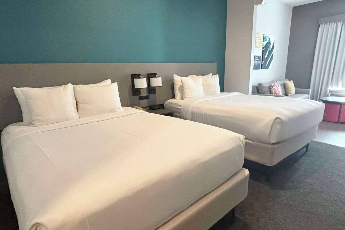 A hotel room with two beds, a nightstand, a lamp, and a window with curtains.