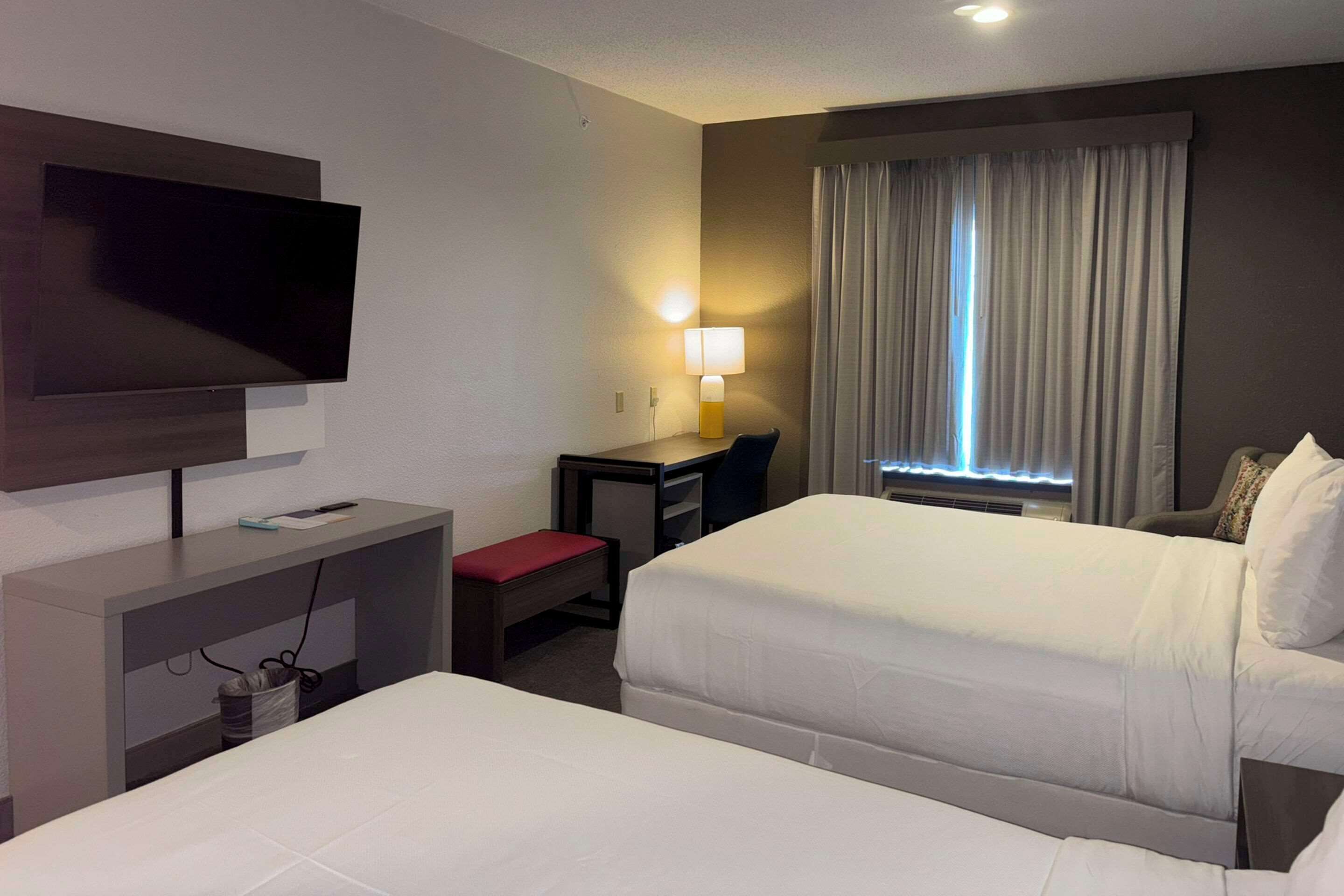 A hotel room with two beds, a desk, a TV, a lamp, and a window with curtains.