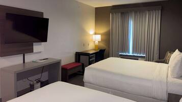 A hotel room with two beds, a desk, a TV, a lamp, and a window with curtains.