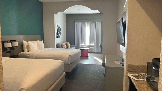 Une chambre d’hôtel avec deux lits, un bureau, une télévision et une fenêtre avec des rideaux.