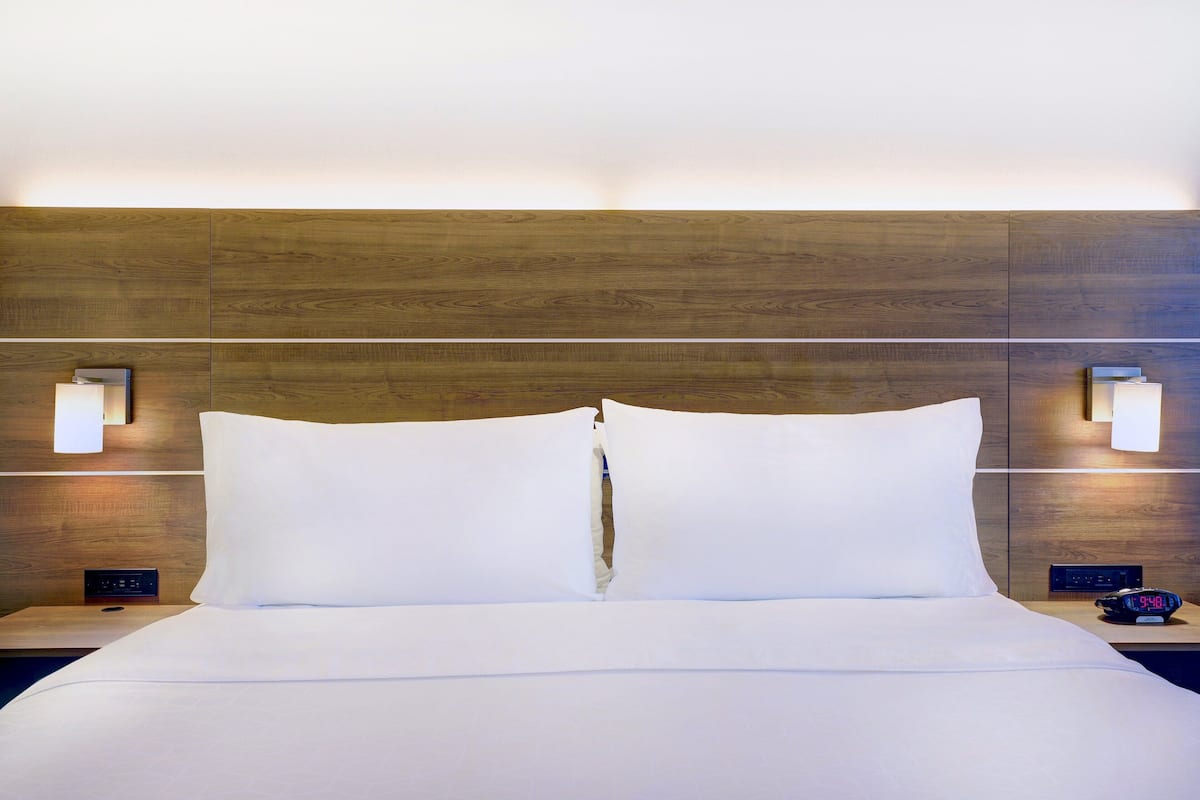 A hotel room with a wooden headboard, white bedding, two bedside lamps, and a digital clock.