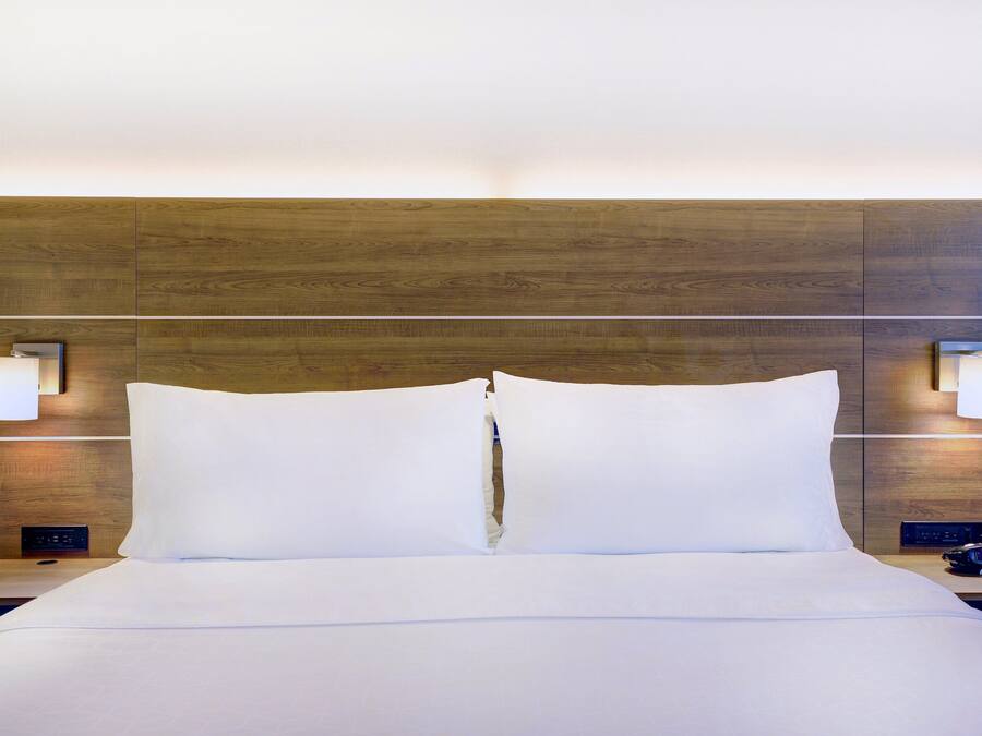 A hotel room with a wooden headboard, white bedding, two bedside lamps, and a digital clock.